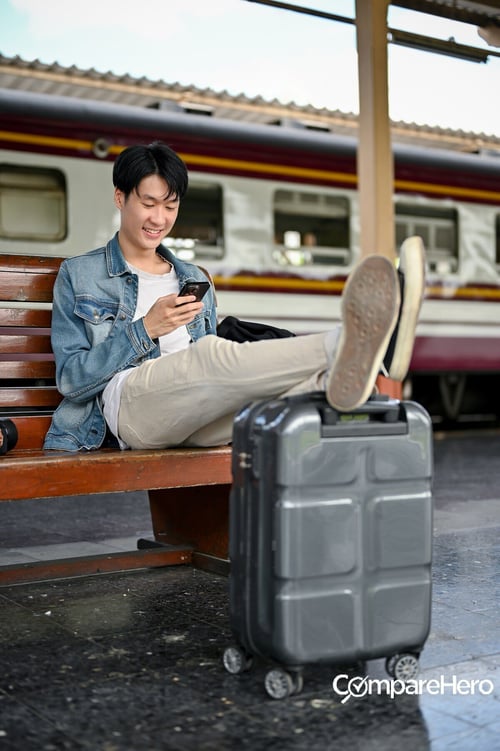 handsome-asian-male-backpacker-using-his-phone-while-waiting-his-train-platform